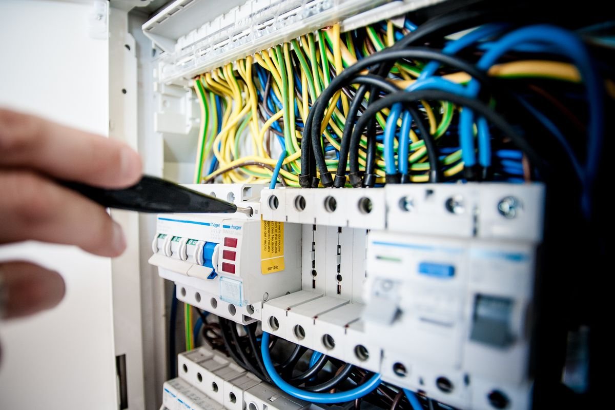 Electrician working inside a circuit breaker panel with colour-coded wires