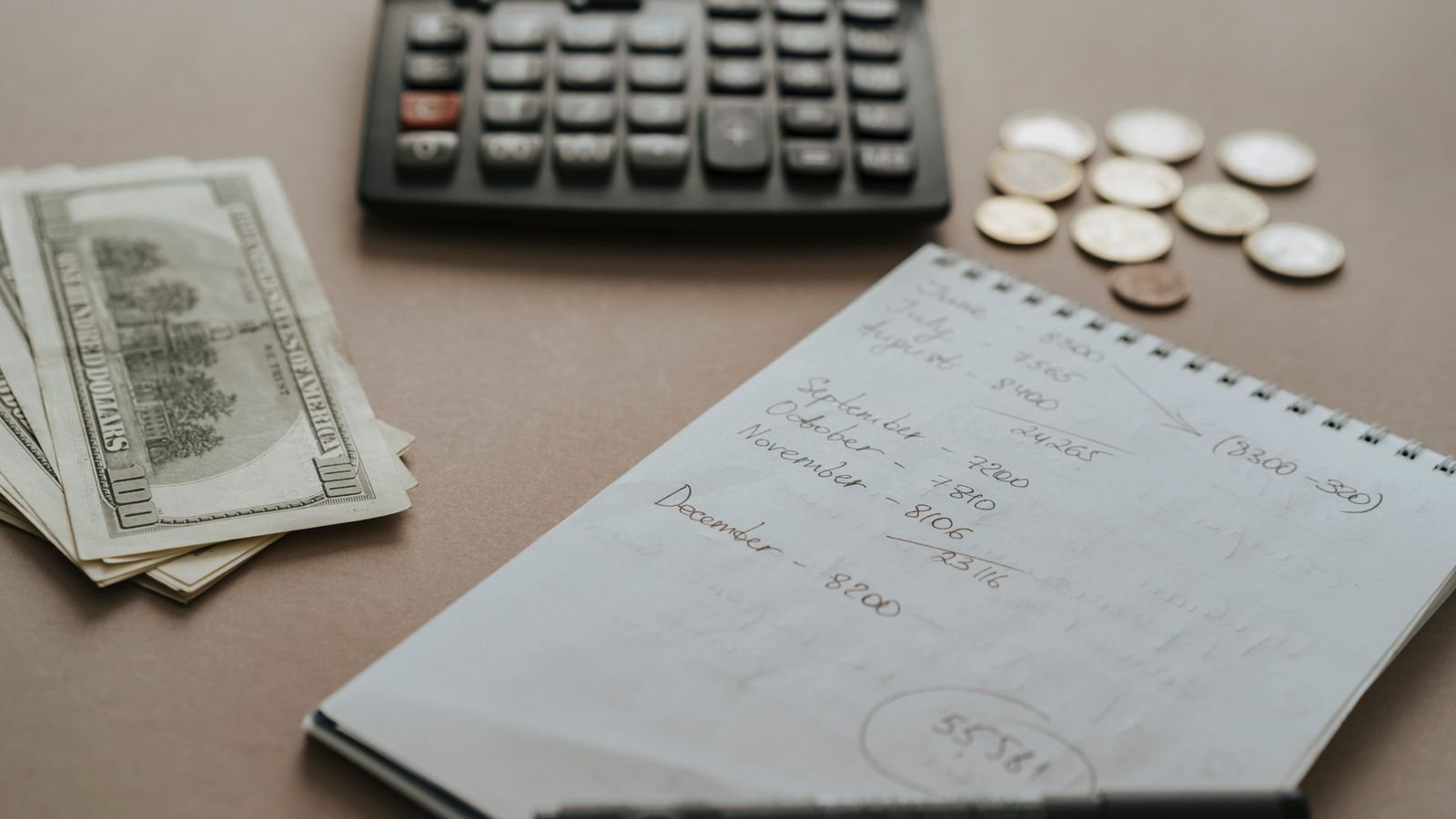 Calculator, notebook and cash laid out on a desk for budgeting a project