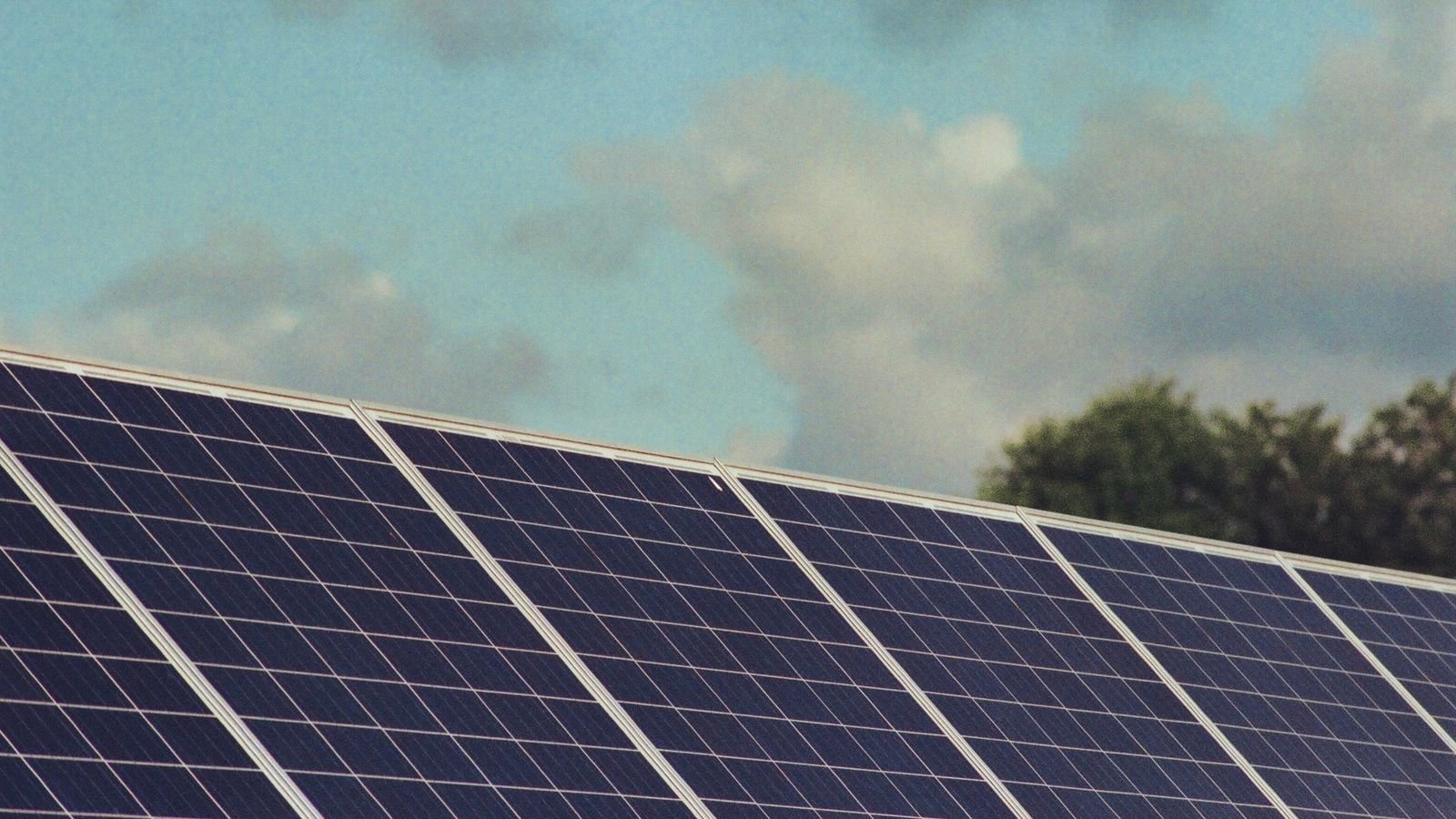 Rows of dark solar panels installed on a roof under a partly cloudy sky