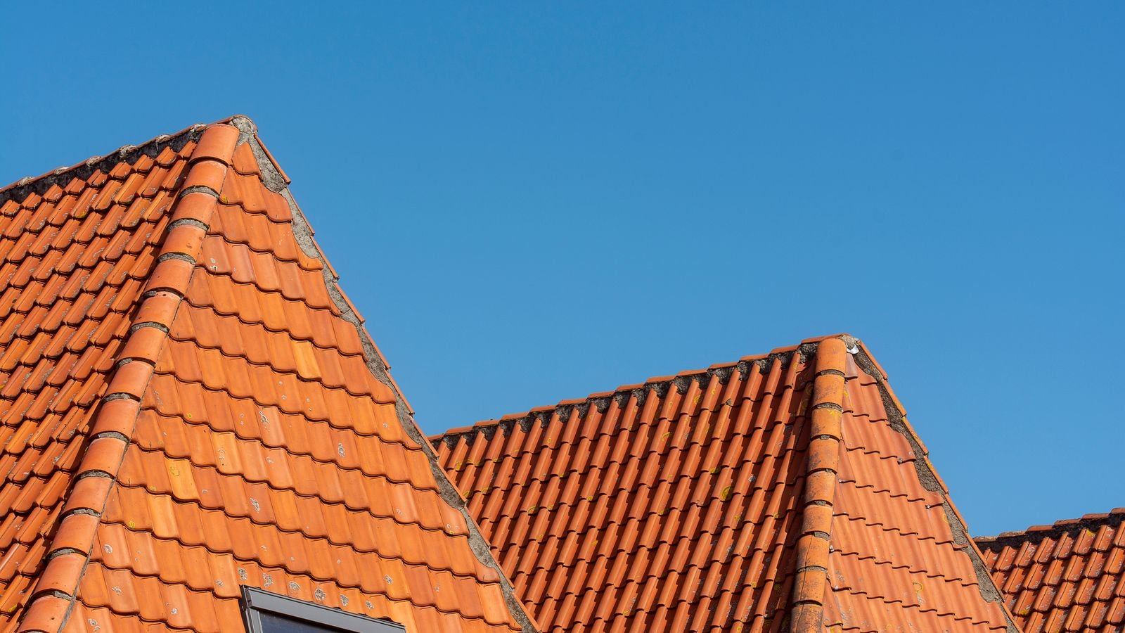 Pitched residential roof against a clear blue sky, viewed from ground level