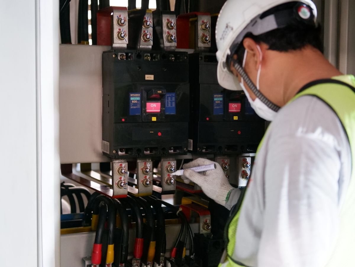 Technician in safety gear inspecting an electrical panel