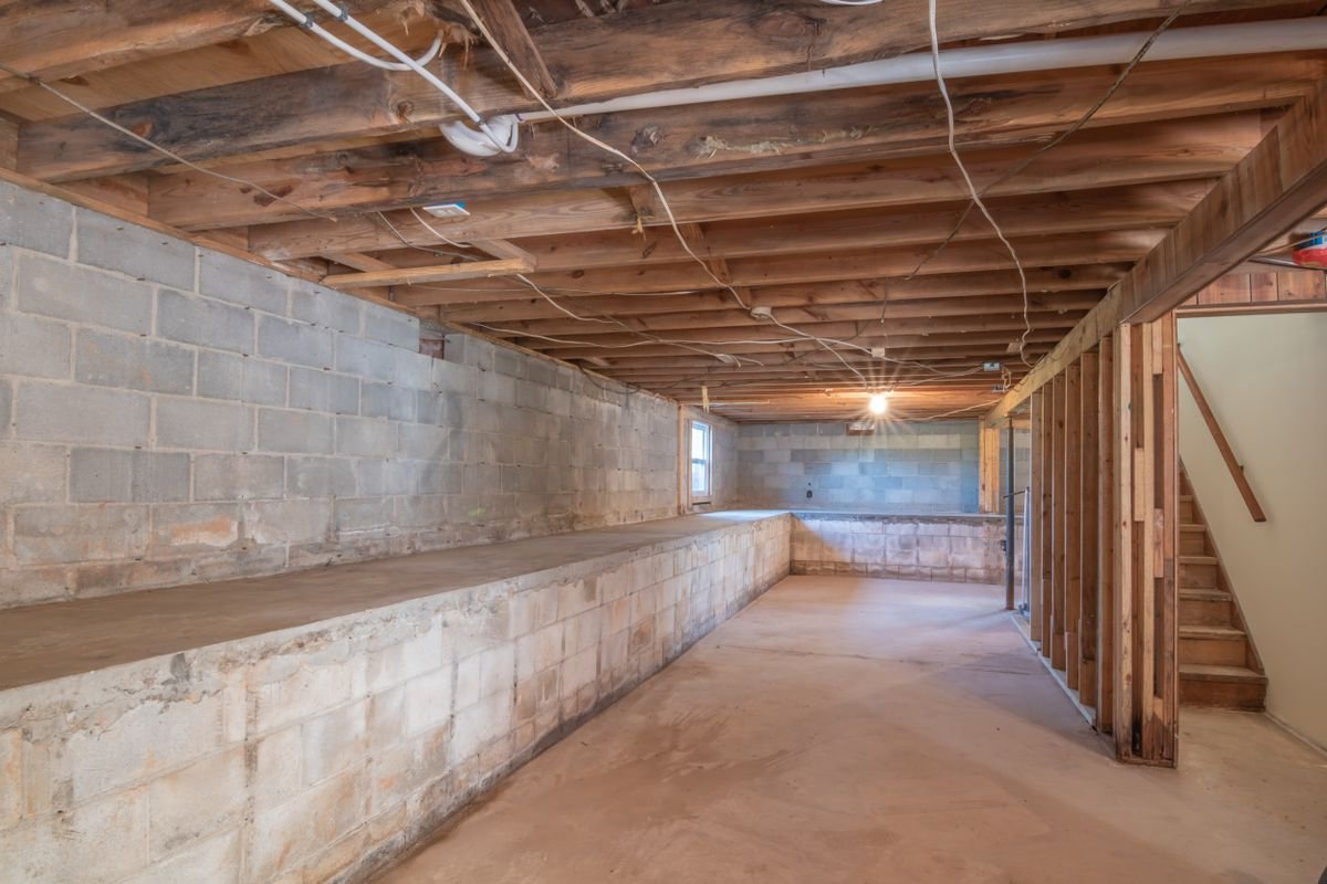 Unfinished basement with exposed wooden beams, concrete walls and stairs