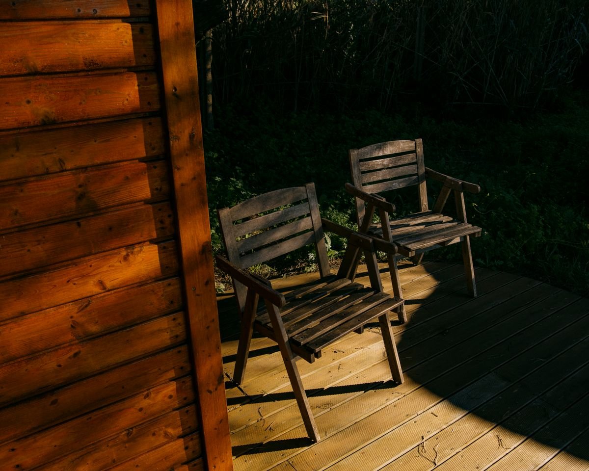 Wooden chairs on a sunlit deck beside a cabin