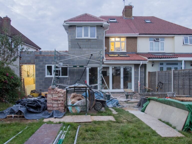 A wood-framed room addition under construction attached to an existing house